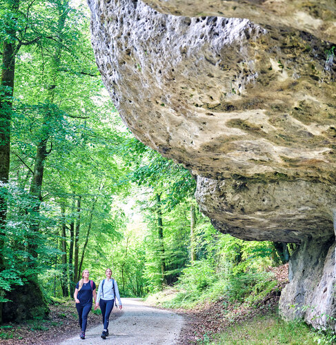 Zwei Frauen wandern unter einem überhängenden Fels hindurch.